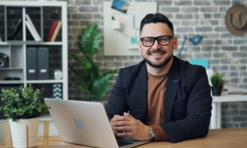 Man smiling while sitting in front of a laptop computer.